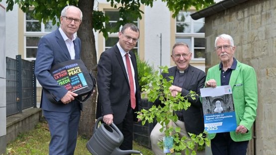 Das Foto zeigt einen jungen Ginkgo-Baum am Forum St. Liborius, der von (v.l.n.r.) Landrat a. D. Manfred Müller, Pfarrer Dr. Eckhard Düker (Evangelischer Kirchenkreis Paderborn), Dechant und Domkapitular Benedikt Fischer (Erzbistum) und Hermann-Josef Bentler als Kreisvorstandsmitglied des Volksbundes) gepflanzt wurde. Pfarrer Dr. Eckhard Düker gießt den Baum noch, während Dechant und Domkapitular Benedikt Fischer den Spaten der Baumpflanzaktion noch in den Händen hält.
